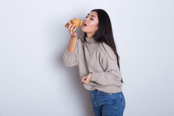 Beautiful and hungry Asian girl eating tasty croissant and smile. Breakfast isolated on white background. Happy young woman have a fun with tasty meal.