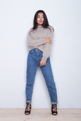 Portrait of looking away serious girl which touch her sweeter and fashion posing on white background.Styling wearing girl in a jeans, shoes and sweeter