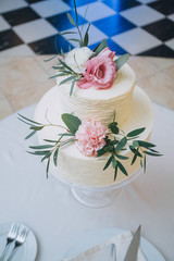 White layered wedding cake decorated with pink roses stands on the table