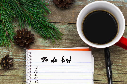  cup of coffee christmas fir tree with cones and notebook with to do list on wooden  background from above. Flat lay style