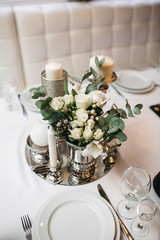Centerpiece made of silver tray, vase with roses and candles stands on the dinner table