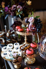 Dishes with cookies, eclairs, macaroons and other sweets made of chocolate and cream served on black table