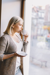 Young woman drinking coffee, looking through the window.