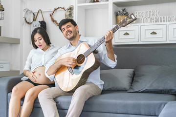 Husband playing guitar with beautiful pregnant in the living room. concept of family relax holiday.