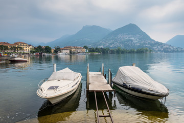 Fototapeta na wymiar Lake and mountains in Lugano, Switzerland. Boats are moored in the foreground.