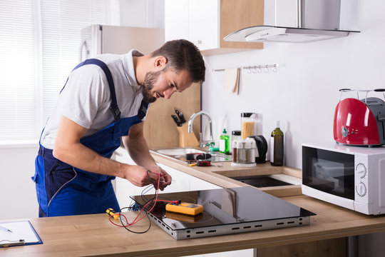 Technician Repairing Induction Stove In Kitchen