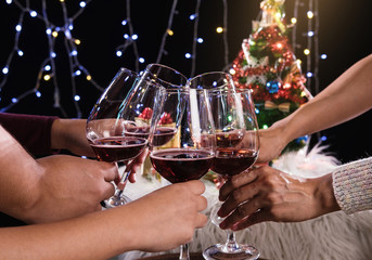 Friends celebrating Christmas or New Year eve party, cheering with wine, christmas lights decoration background, christmas atmosphere