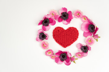 Red knitted heart surrounded by pink flowers.