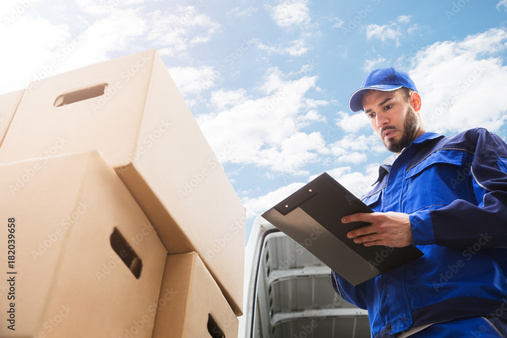 Wall mural Male Worker Standing Near Cardboard Box Holding Clipboard