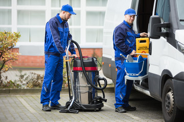 Two Male Janitor Unloading Cleaning Equipment From Vehicle