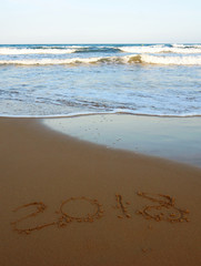 New Year 2018 is written on the sand on the beach with an incoming foaming wave, vertical