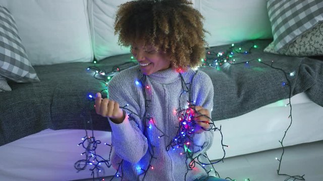 Wonderful pretty woman with curls smiling cheerfully at camera posing with blue lights of garland glowing in dark.
