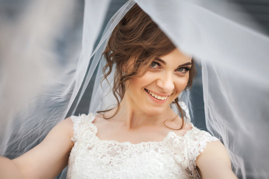 Portrait of beautiful smiling bride with white veil over her face. Concept of young gorgeous bride.