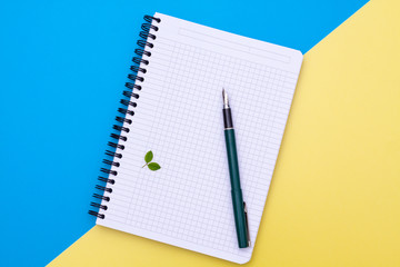 Top view on a blank notebook with pen flat lay on blue and yellow background.