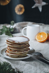A still life of breakfast scene, that includes traditional american pancakes topped with maple syrop and sugar powder, a cup of black coffee and oranges