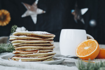 A still life of breakfast scene, that includes traditional american pancakes topped with maple syrop and sugar powder, a cup of black coffee and oranges