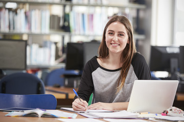 Portrait Of Female Student Working At Laptop In College Library