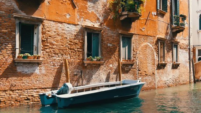 VENICE, ITALY, SEPTEMBER 7, 2017: a cozy wall of a Venetian brick house next to a parked boat and passing by a canal another boat with people