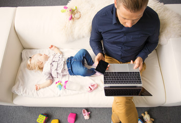 Dad working on laptop while his baby girl sleeping on the couch