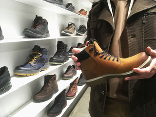 Young man buy or choose winter shoes in shoe store