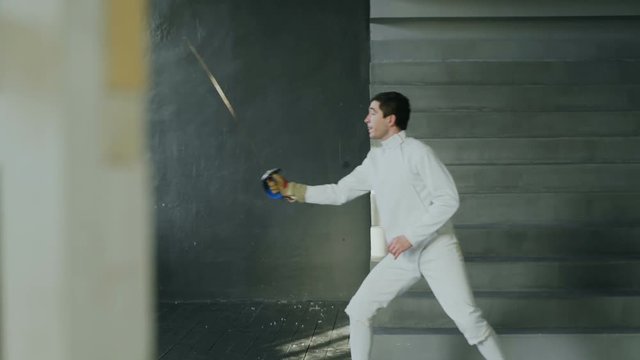 Young concentrated fencer man practice fencing exercises and training for Olympic games competition in studio indoors