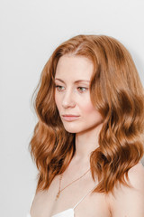 Obraz premium Ginger woman with wavy volumetric hair styling at white background