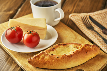 Traditional georgian cheese pie khachapuri with tomatoes and cup of steaming tea or coffee on wooden table