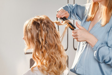 Fototapeta premium Straightening and curling of blonde hair in hairstyle salon with iron