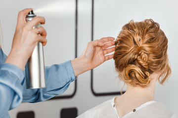 An coiffeur in the hairdressing salon makes a hairstyle and fixes it with a spray