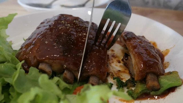 Steak, pork ribs and chef are cut with knife and fork in white plate. Video