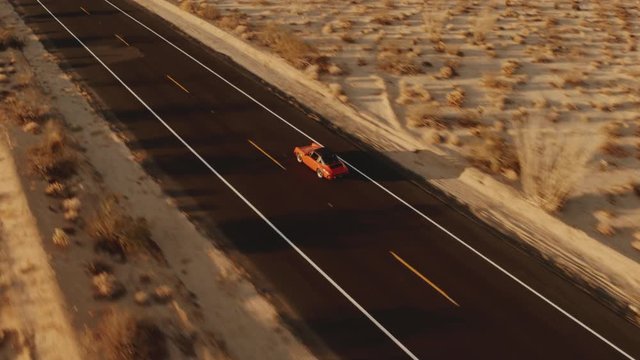 Aerial View Red Classic Car Driving Along Desolate Desert Road At Sunset