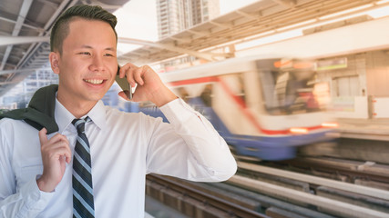 The portrait of young Asian executive using smartphone at sky train terminal