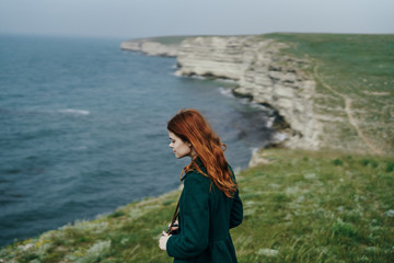 Young beautiful woman on a cliff of a mountain near the sea, the wind blows