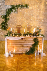 catering, dining, wedding concept. in the shining dining hall with walls decorated by twinkle lights there are table for bride and groom, surrounded by burning candles