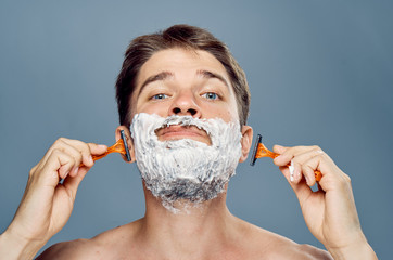 Man with a beard on a gray background in shaving foam shaving, portrait