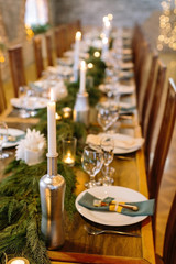 wedding decor, interior, illumination concept. close up of served holiday table with candles in original holders that looks like bottles, among them there are fresh branches of conifer trees