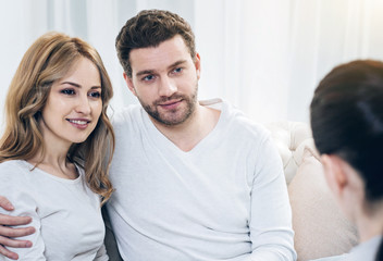 Obraz premium Overcoming problems. Joyful nice positive couple sitting together and looking at their therapist while feeling happy