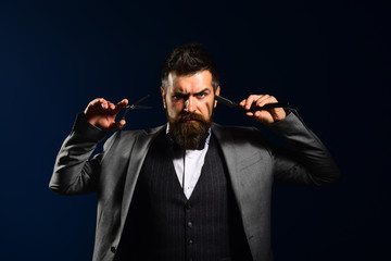 Man with long beard holds shaving razor and scissors.