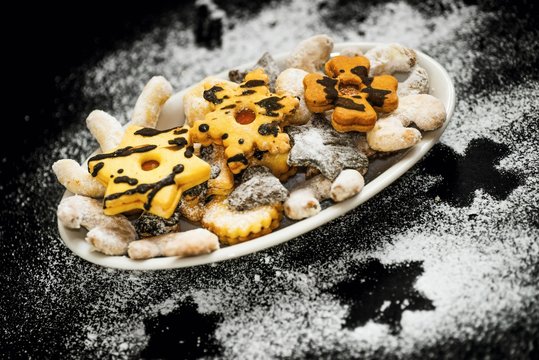 Plate with mix of christmas ckaes on black background sprinkled with sugar.