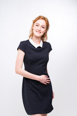 beautiful young girl student, secretary or business lady with charming smile and red curly hair in black dress in white dot and white collar on white gray background in studio