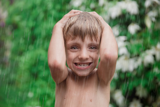 Cheerful, excited baby having fun, running wet under rain