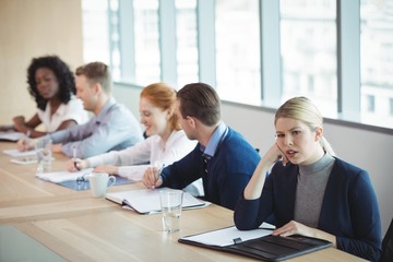 Thoughtful businesswoman sitting with colleagues at desk