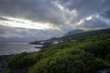 lava coastline with a volcano under a dramatic sky at sunset on the island of Pico on the azores © Vladimira