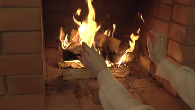 Девушка греет руки у камина. 