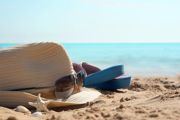 Hat with sunglasses and beach slippers on the sand against the blue sea