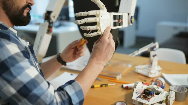 Creating masterpiece. Close up of enthusiastic constructor using a screwdriver and being attentive while repairing robots hand