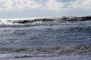 Storm wave rolls to the shore in the shadow of the clouds