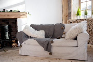 white sofa with fluffy pillows and a coverlet with pompoms near the fireplace, Scandinavian style