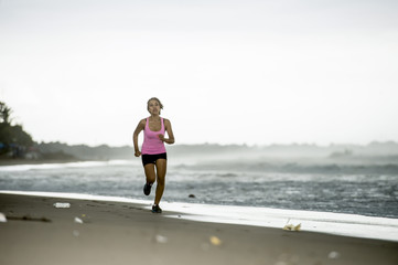 Fototapeta na wymiar young attractive and fit Asian sport runner woman running on beach sea side smiling happy in fitness