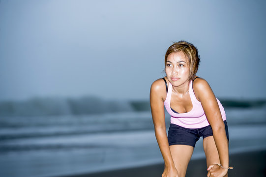 fit Asian sport runner woman cooling off breathing after running on beach sea side looking tired while hard workout